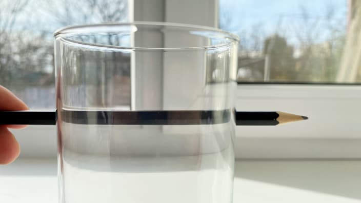 creionul arată distorsionat din cauza că paharul refractă lumina